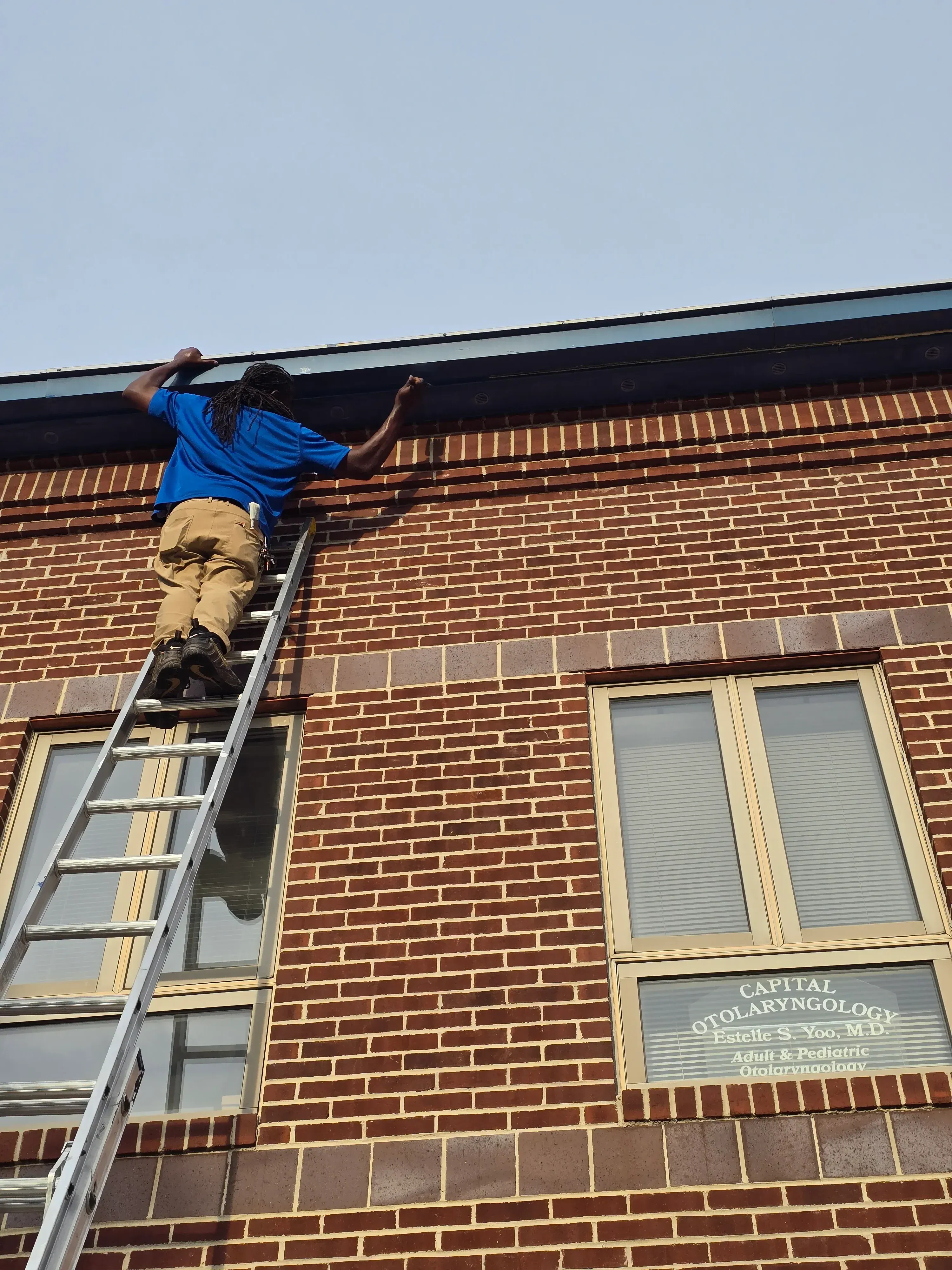 Pest control technician treating brick building exterior with spray application near windows